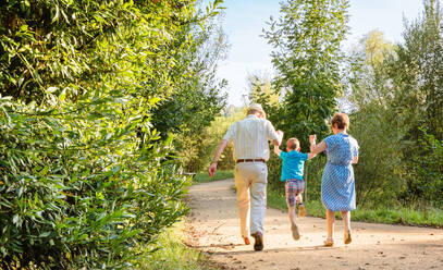 Back view of grandparents and grandchild jumping on a nature path - ADSF50048