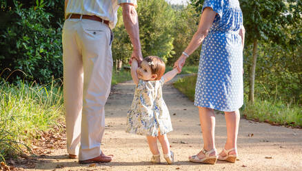 Portrait of baby granddaughter walking with her grandparents on a nature path - ADSF50050