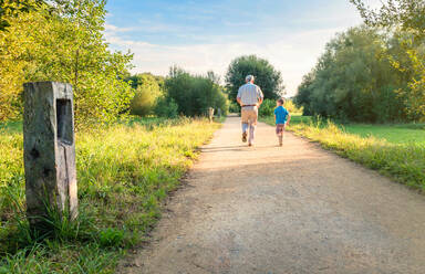 Back view of senior man with hat and happy child running on a nature path. Two different generations concept. - ADSF50053