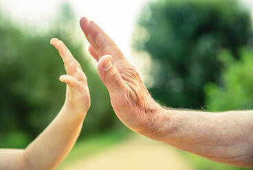 Child and senior man hands giving five over a nature background. Two different generations concept. - ADSF50061