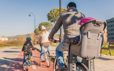 Back view of happy family with children riding bicycles by the nature on a sunny winter day - ADSF50067