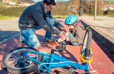 Father putting a plaster band over knee injury to his son after falling off to the bicycle - ADSF50069