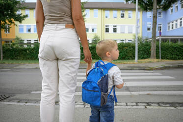 Legs of a young caucasian woman in cropped jeans and sneakers, holding hands with toddler, looking before crossing street while going to kindergarten - ADSF50096