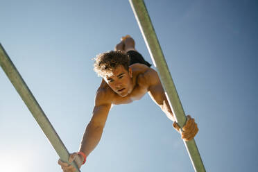 Handsome young man with blond hair shirtless doing handstands on parallel bars at an outdoor calisthenics park on a sunny day - ADSF50172