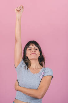 Eine glückliche Frau, die eine rosafarbene Schleife zur Sensibilisierung für Brustkrebs trägt, hebt ihren Arm und zeigt damit den Kampf gegen Brustkrebs - ADSF50183