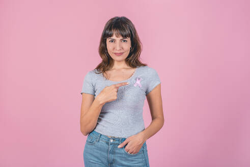 Eine Frau, die auf eine rosa Brustkrebsschleife auf ihrem T-Shirt zeigt. - ADSF50184
