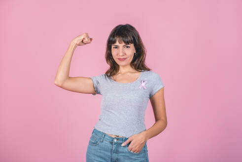 Eine Frau, die ein rosa Brustkrebs-Band trägt und ihre Armmuskeln zeigt: Sieg über Brustkrebs. - ADSF50185