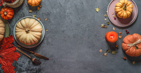 Top view of autumn background frame with various pumpkins, red fall leaves, plates, cutlery and candle at dark grey backdrop - ADSF50187