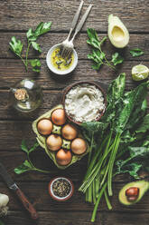 Preparing spinach ricotta stuffing with herbs, eggs and spices at dark wooden kitchen table. Cooking at home with fresh healthy ingredients. Top view. - ADSF50192