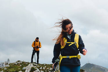 Kaukasische Frau mit windverwehtem Haar wandert mit ihrem Partner. Wandern an einem bewölkten Tag. Outdoor-Sport - ADSF50202