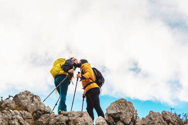 Hiker couple with backpack and trekking poles kiss after reaching a mountain peak. two lovers hiking. - ADSF50203