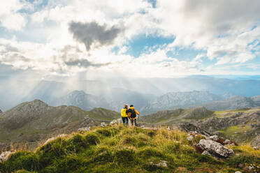 Paar Wanderer mit Rucksäcken, stehend und umarmend auf dem Gipfel eines Berges mit Blick auf die Landschaft der Bergkette. Sport und Outdoor-Aktivitäten. - ADSF50208