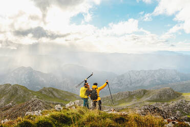Zwei Wanderer mit Rucksäcken, die ihre Trekkingstöcke hochheben, als sie den Gipfel eines Berges erreichen. Bergsteiger, die die Landschaft der Bergkette betrachten - ADSF50209