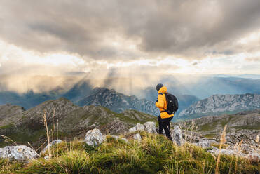 Unbekannte Person mit Rucksack, oben auf einem Felsen, die Landschaft betrachtend, nachdem sie einen Berg bestiegen hat. Wanderer, der an einem bewölkten Tag einen Gipfel erreicht. - ADSF50218