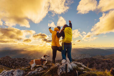 Ein Wanderpärchen mit ihrem Hund, das den Sonnenuntergang vom Gipfel eines Berges aus beobachtet. Sport und Aktivitäten in den Bergen und im Freien. - ADSF50230