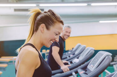 Beautiful fitness woman laughing with friend in a treadmill training on fitness center - ADSF50243