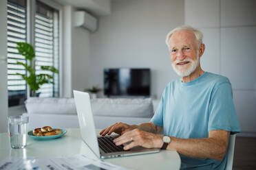 Älterer Mann im Rollstuhl, der im Ruhestand von zu Hause aus arbeitet. Älterer Mann, der digitale Technologien nutzt und an einem Laptop arbeitet. Konzept von Senioren und digitalen Fähigkeiten. - HPIF34201