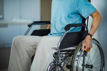 Nahaufnahme eines älteren Mannes, der zu Hause in einem Rollstuhl sitzt und die Räder mit den Händen festhält. - HPIF34206