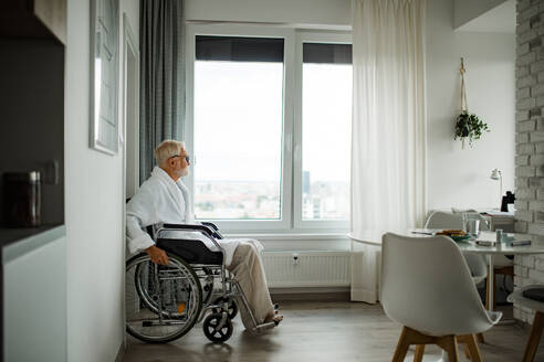 Senior man in a wheelchair spends time alone in his apartment. Concept of loneliness and dependence of retired people. - HPIF34214