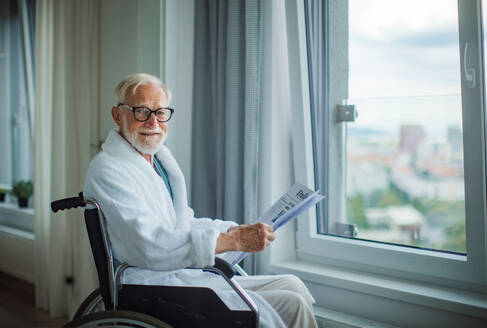 Älterer Mann im Rollstuhl, der morgens im Morgenmantel die Zeitung liest. Konzept der Einsamkeit und Abhängigkeit von Menschen im Ruhestand. - HPIF34216
