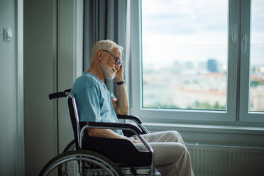 Senior man in a wheelchair spending time alone in his apartment. Concept of loneliness and dependence of retired people. - HPIF34218