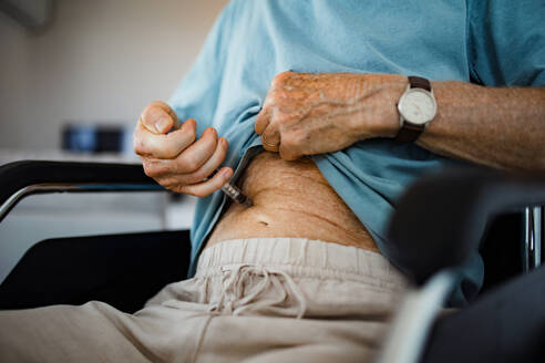 Diabetischer älterer Patient, der sich Insulin in den Bauch spritzt. Nahaufnahme eines älteren Mannes im Rollstuhl mit Typ-1-Diabetes, der Insulin mit einer Spritzennadel einnimmt. - HPIF34226