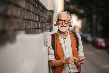 Close up shot of a senior man on the street. Elderly cool man listening to music outdoors, having fun. Concept of old man young at heart. - HPIF34257