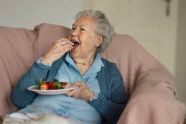 Eine ältere Frau ruht sich in ihrem Haus aus und isst Erdbeeren. - HPIF34277