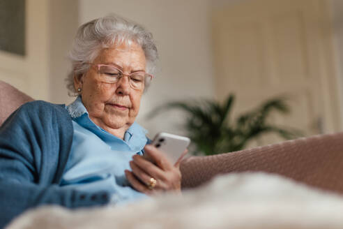 Porträt einer älteren Frau, die auf ihrem Smartphone surft. Ältere Frau, die zu Hause ein Mobiltelefon benutzt. - HPIF34278