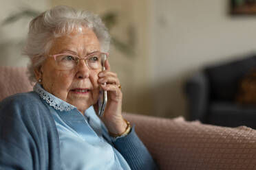 Porträt einer älteren Frau, die zu Hause sitzt und telefoniert. - HPIF34279