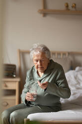 Eine ältere Frau sitzt auf ihrem Bett und nimmt Tabletten. - HPIF34283