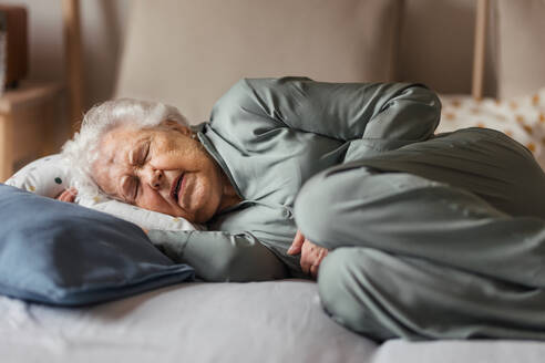 Ältere Frau schläft allein in ihrem Bett. Frau mit Schmerzen und Angstgefühlen. Einsamkeit und soziale Isolation einer älteren Frau. - HPIF34288