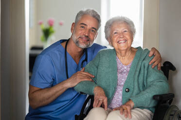 Portrait of caregiver with patient, senior woman in her home. Thoughful male nurse taking care of eldery patient on wheelchair. - HPIF34297