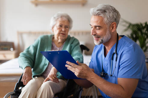 Pflegerin bei der regelmäßigen Untersuchung einer älteren Klientin in ihrem Haus. Fürsorglicher Pfleger, der sich um eine ältere Patientin im Rollstuhl kümmert. - HPIF34301