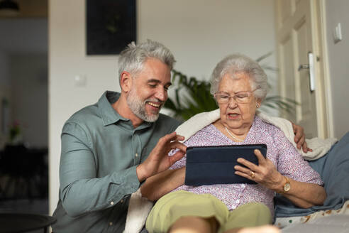 Älterer Mann lernt seine ältere Mutter bei der Arbeit mit einem digitalen Tablet. - HPIF34345