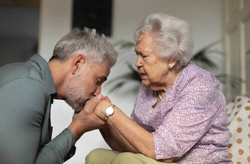 Porträt eines reifen Mannes mit seiner älteren Mutter. Der Sohn küsst die Hände seiner Mutter. Gemeinsame Bewältigung von Trauer und Verlust. - HPIF34347