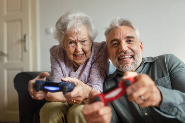 Mature man visiting his senior mother at her home, playing video games together. - HPIF34351