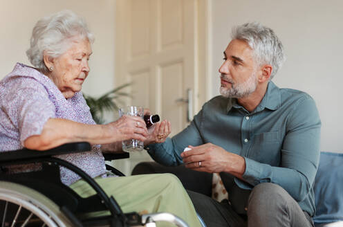 Close up of adult son giving pills to his ill mother. Taking prescribed medication. Helping senior take medication safely, at the right time. - HPIF34354