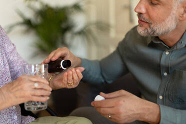 Close up of adult son giving pills to his ill mother. Taking prescribed medication. Helping senior take medication safely, at the right time. - HPIF34355