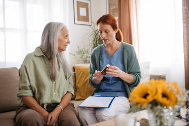 Krankenschwester gibt einer älteren Frau zu Hause Tabletten. - HPIF34360