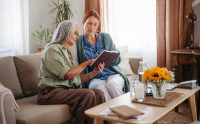 Ältere Frau und Krankenschwester lesen zusammen ein Buch und haben eine schöne Zeit zu Hause. - HPIF34373