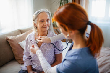 Krankenschwester untersucht älteren Patienten mit Stethoskop zu Hause. - HPIF34397