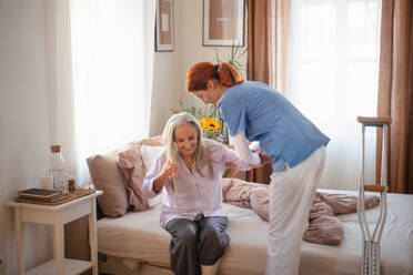 Krankenschwester, die einer älteren Frau nach einer Beinverletzung beim Gehen hilft, in ihrer Wohnung. - HPIF34404