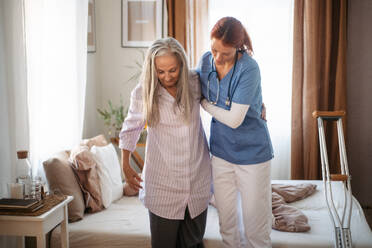 Krankenschwester, die einer älteren Frau nach einer Beinverletzung beim Gehen hilft, in ihrer Wohnung. - HPIF34405