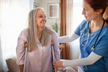 Krankenschwester, die einer älteren Frau nach einer Beinverletzung beim Gehen hilft, in ihrer Wohnung. - HPIF34407