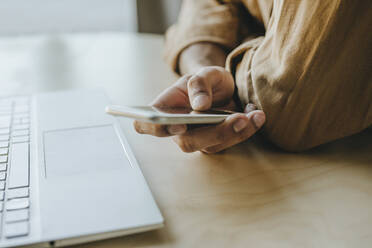 Young man text messaging through mobile phone on table at home - YTF01482