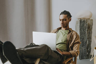 Young man using laptop sitting with feet up on table relaxing at home - YTF01487