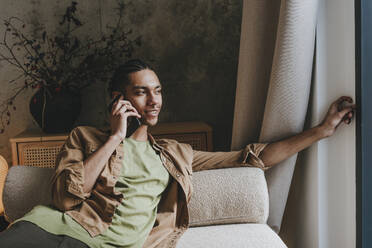 Junger Mann spricht mit seinem Smartphone auf dem Sofa zu Hause - YTF01497