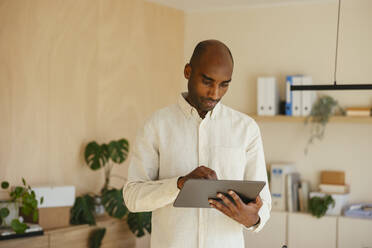 Confident businessman using digital tablet standing at home office - EBSF04237