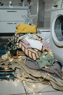 Christmas tree made from heap of laundry clothes near washing machine - ANAF02526